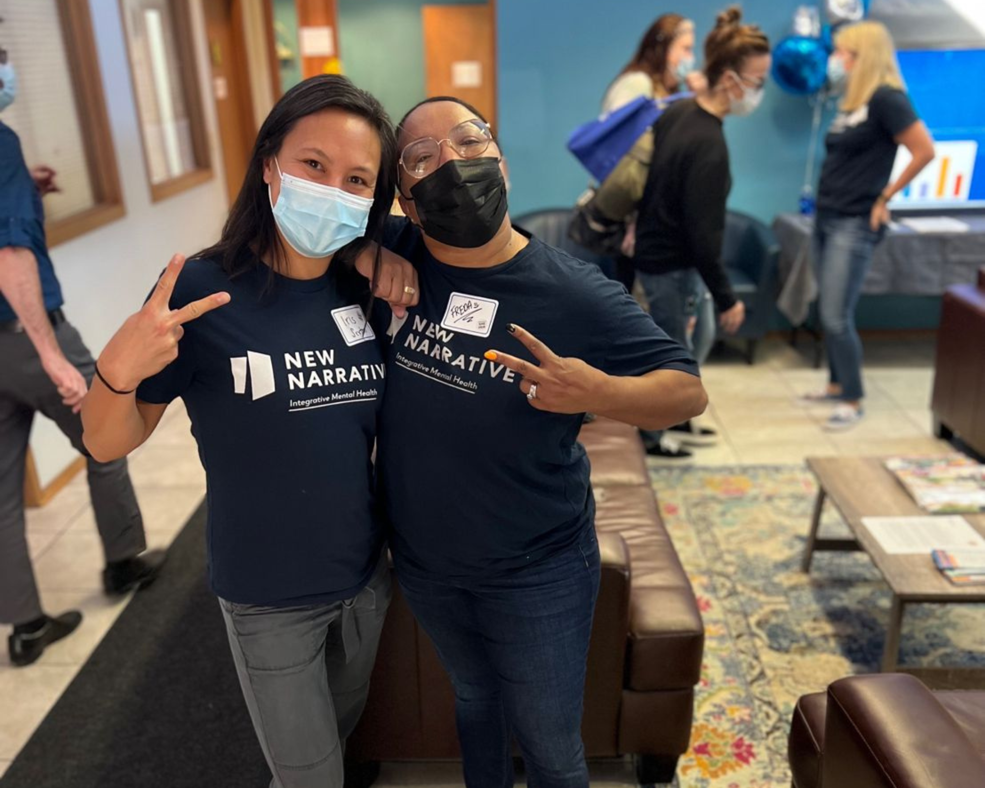 two New Narrative staff, both BIPOC women, throw peace signs at the camera while wearing their dark blue New Narrative tshirts.