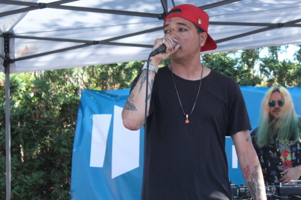 artist rapping onstage, wearing a black shirt and backwards red cap