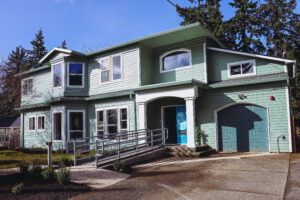 Exterior of Jade House, a 2-story residence with seafoam green paint and a ramp up to the front door