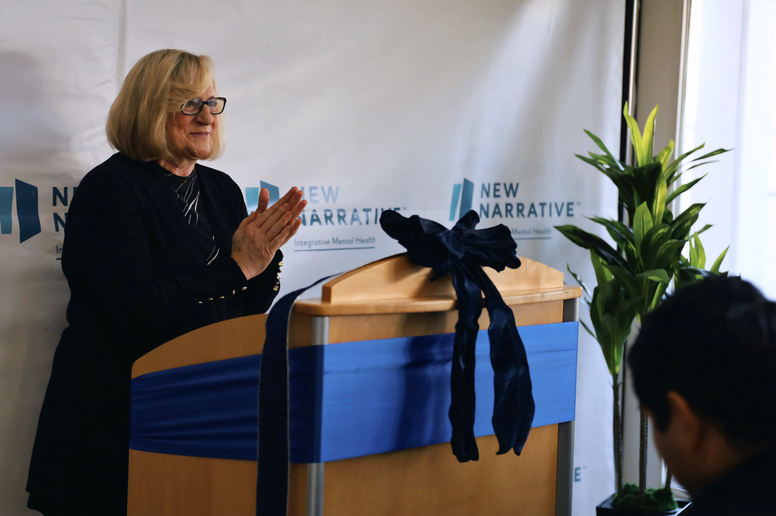 CEO Julie Ibrahim claps at a podium for a New Narrative grand opening
