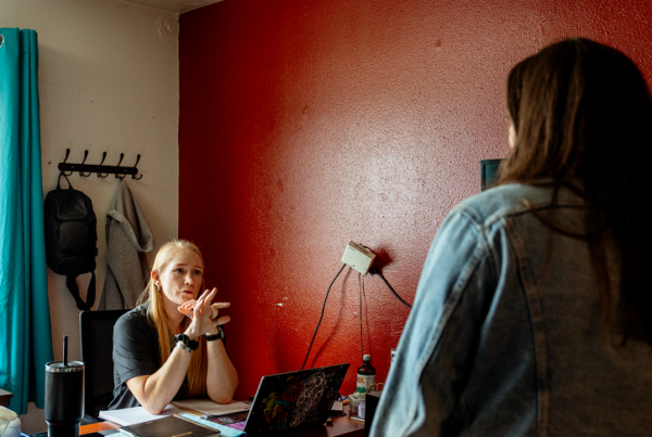 Wendie Smith, housing specialist at New Narrative, sits at her desk while speaking with a resident. The wall to Wendie's left is accented red.