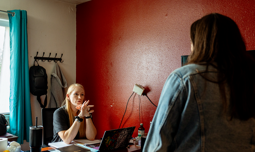 Wendie Smith, housing specialist at New Narrative, sits at her desk while speaking with a resident. The wall to Wendie's left is accented red.